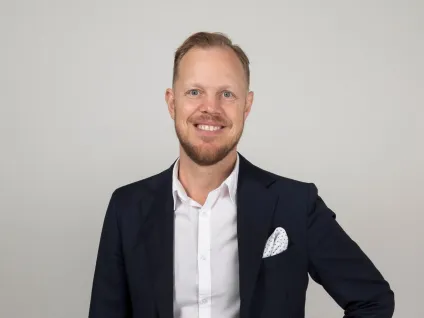 Fredrik Rosenqvist i mörkblå kostym mot grå bakgrund
