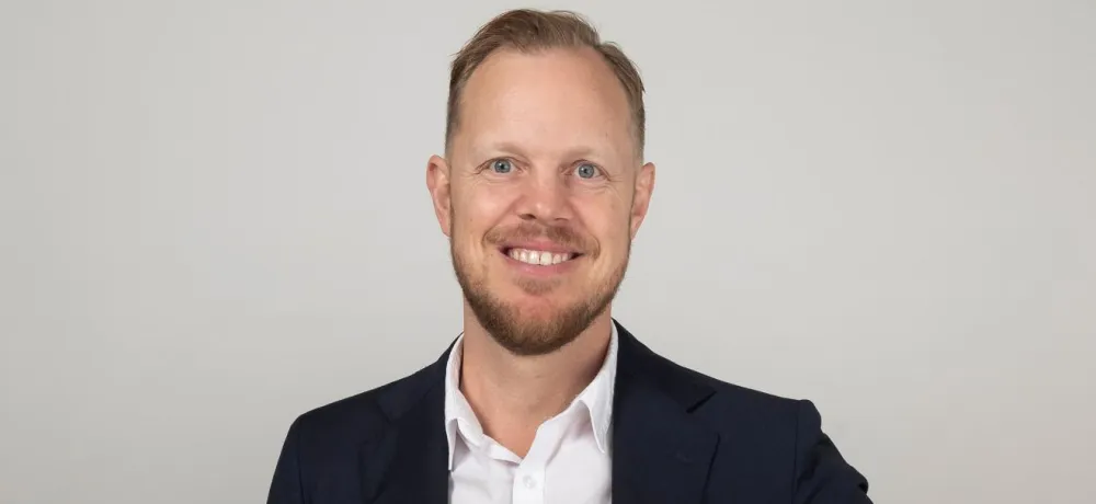 Fredrik Rosenqvist i svart kavaj, vitskjorta mot grå bakgrund
